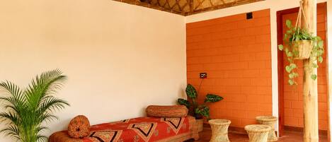 A room with a thatched roof, a sofa with patterned cushions, a potted plant, and wicker furniture.
