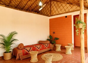 Una habitación con techo de paja, un sofá con cojines estampados, una planta en maceta y muebles de mimbre.
