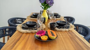 A wooden dining table with black plates, a yellow vase with purple flowers, and a plate of dragon fruit and papaya. - Lasterra Villa (Kerobokan)