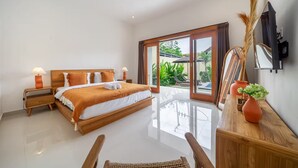 A spacious bedroom with a large bed, a wooden nightstand, a desk, and a view of the outdoors through a sliding glass door. - Lasterra Villa (Kerobokan)