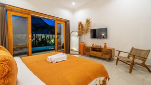 A bedroom with a large bed, a TV, a wooden dresser, a wicker chair, and a view of the outdoors. - Lasterra Villa (Kerobokan)