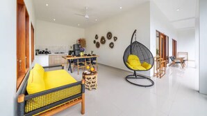 A modern living room with a dining area, a hanging chair, and a kitchen in the background. - Lasterra Villa (Kerobokan)