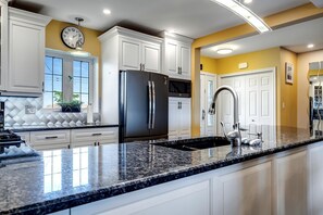 A modern kitchen with white cabinets, a stainless steel refrigerator, a granite countertop, and a built-in microwave. - Lakeside Vacation Rental on Lake Erie for a Unique Escape in Leamington, Ontario (Leamington)
