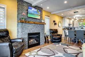 A living room with a stone fireplace, leather chairs, a TV, and a kitchen area with modern appliances. - Lakeside Vacation Rental on Lake Erie for a Unique Escape in Leamington, Ontario (Leamington)