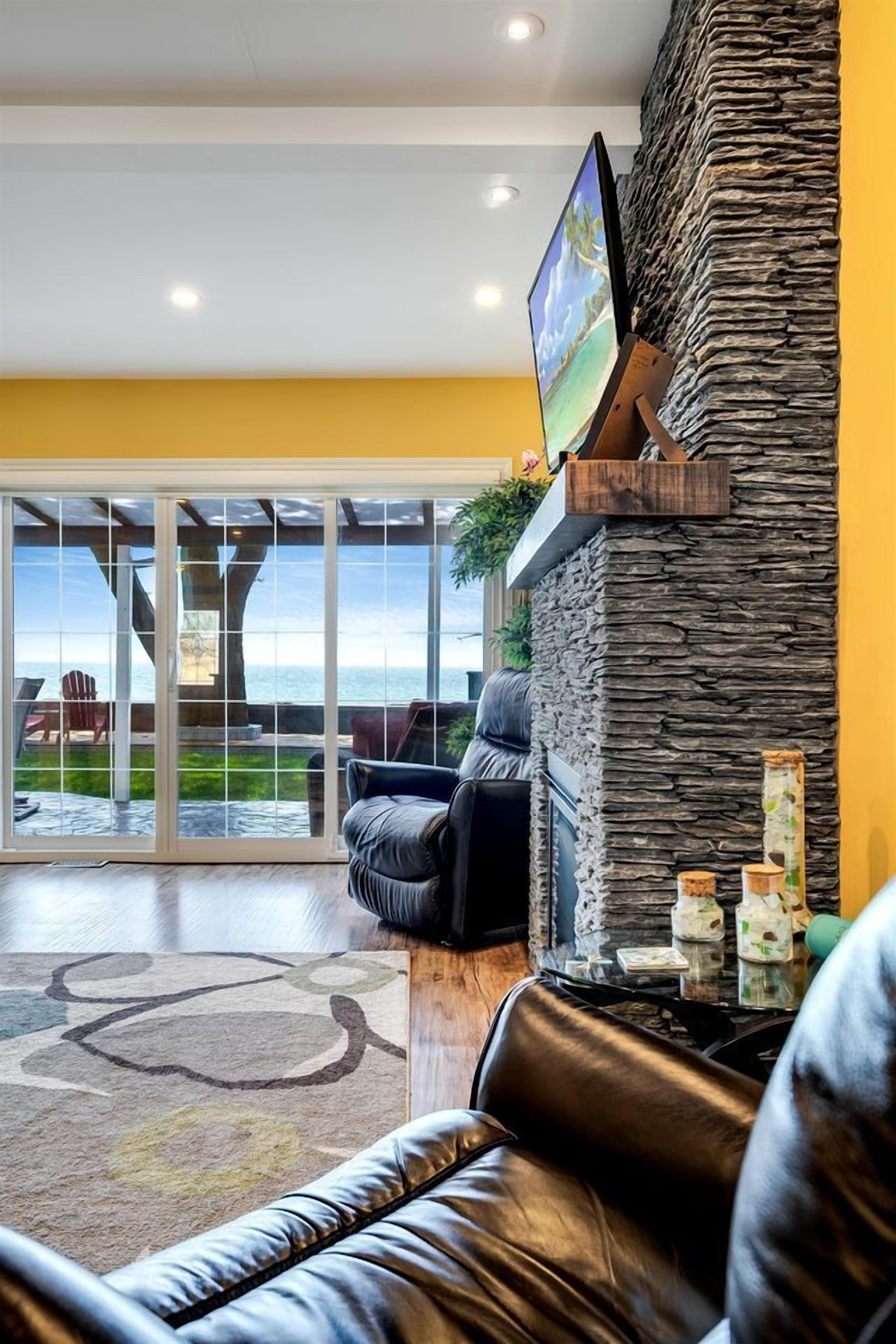 A modern living room with a stone accent wall, a flat-screen TV, a leather sofa, and a view of the outdoors through large glass doors.
