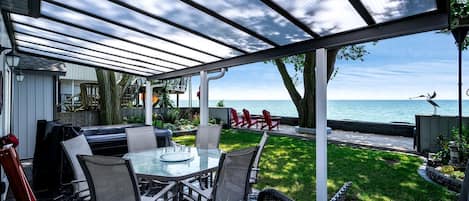 An outdoor patio with a glass table and chairs, a barbecue grill, and a view of the ocean.