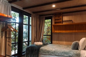 Ein Schlafzimmer mit Bett, einer Kleiderstange, einem Fenster mit Vorhängen und einem Holzregal.
