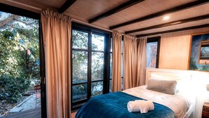 Quarto com uma janela grande, uma cama com cobertor azul e cabeceira.