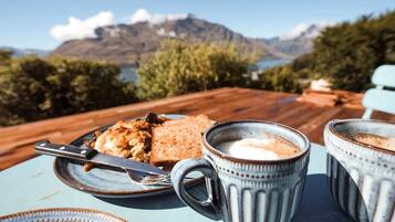 A table with a plate of food, a knife, and two mugs, set against a scenic mountain backdrop.