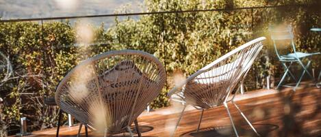 Two wireframe chairs on a wooden deck with a view of trees and hills.