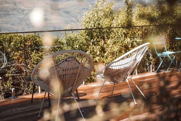 Two wireframe chairs on a wooden deck with a view of trees and hills.