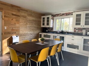 Una cocina moderna con una pared de madera, armarios blancos y una zona de comedor con mesa y sillas.