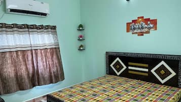 A bedroom with a bed, an air conditioner, a curtain, and a wall-mounted shelf with decorative items.