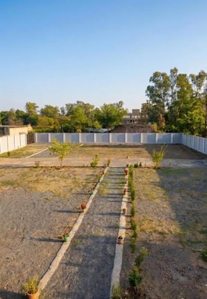 Área externa com calçada pavimentada, vasos de plantas e cerca branca.