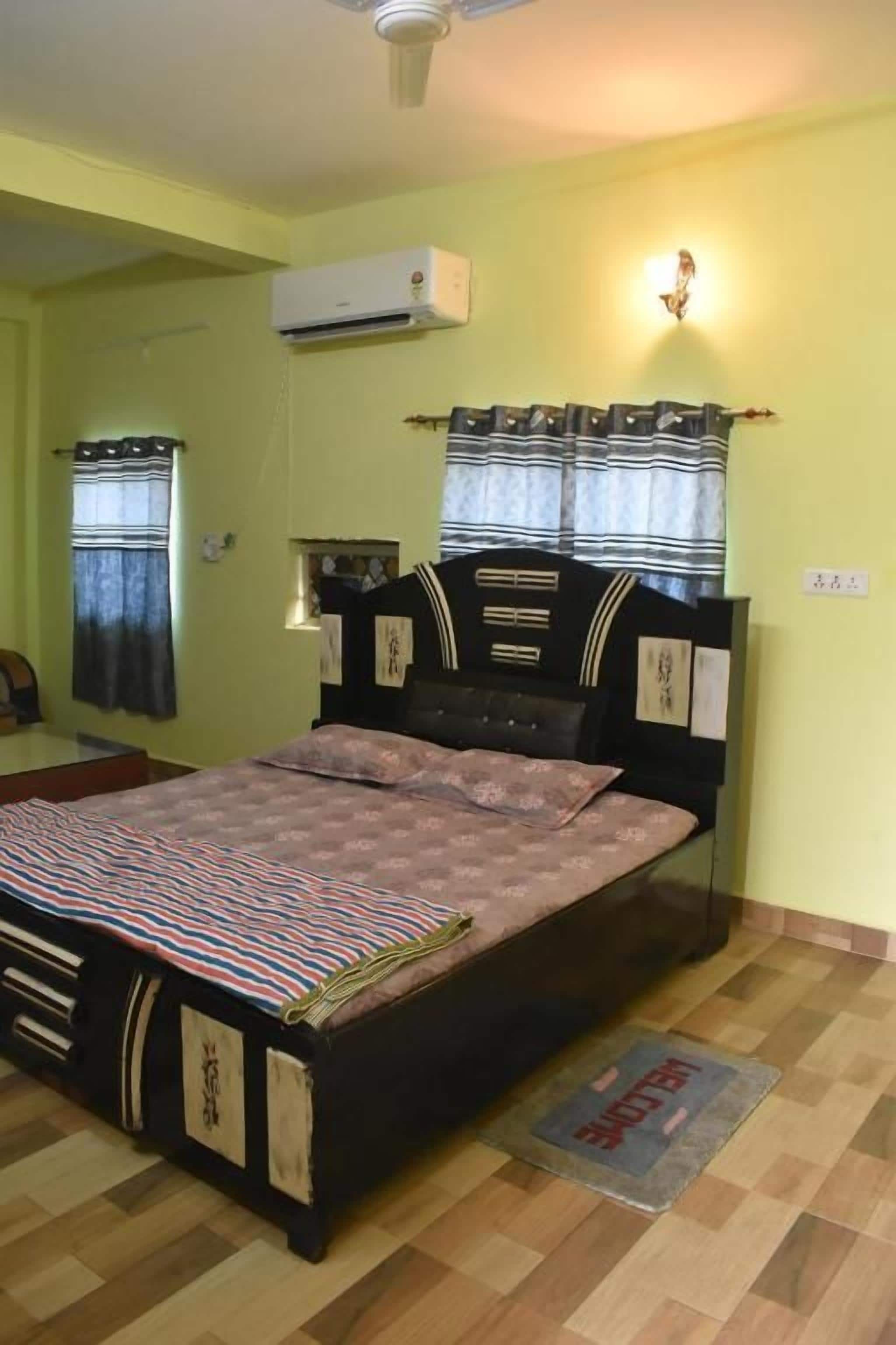 Un dormitorio con cama, ventilador de techo, aire acondicionado y ventana con cortinas.