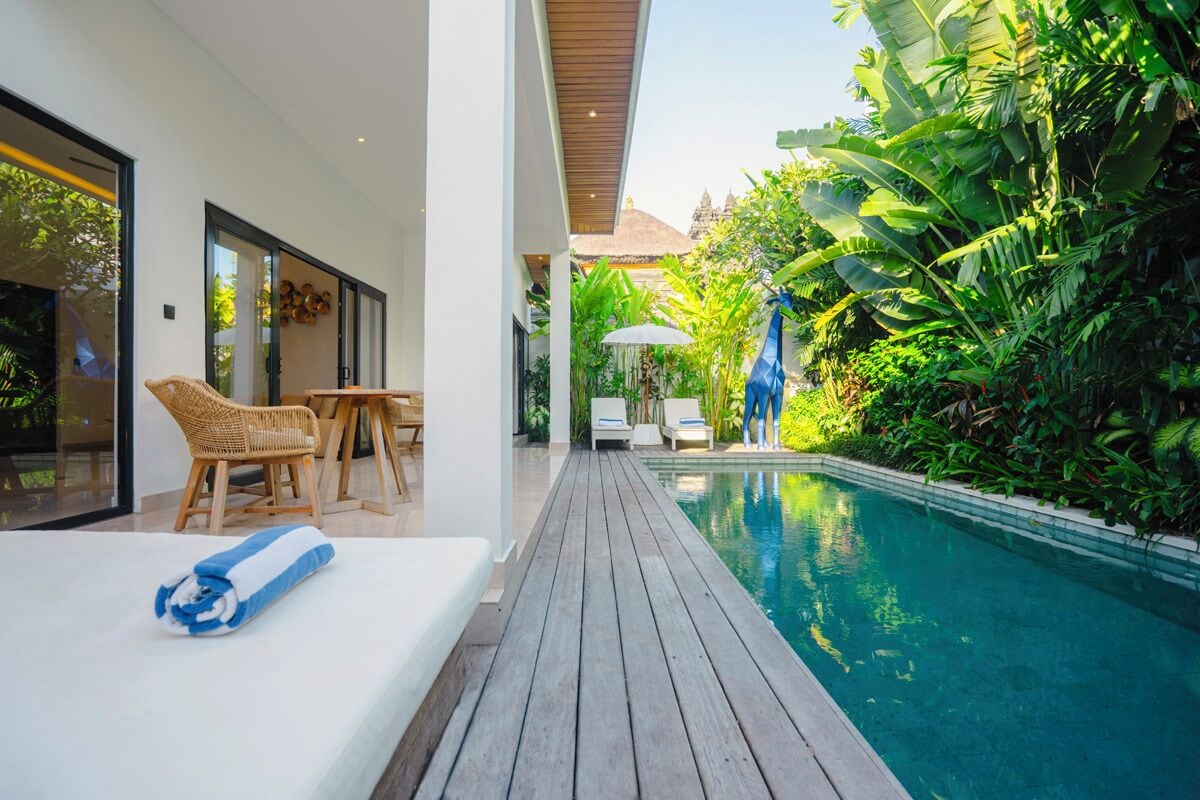 Uma área de piscina moderna com um deck de madeira, espreguiçadeiras e vegetação exuberante.