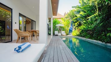 Uma área de piscina moderna com um deck de madeira, espreguiçadeiras e vegetação exuberante.