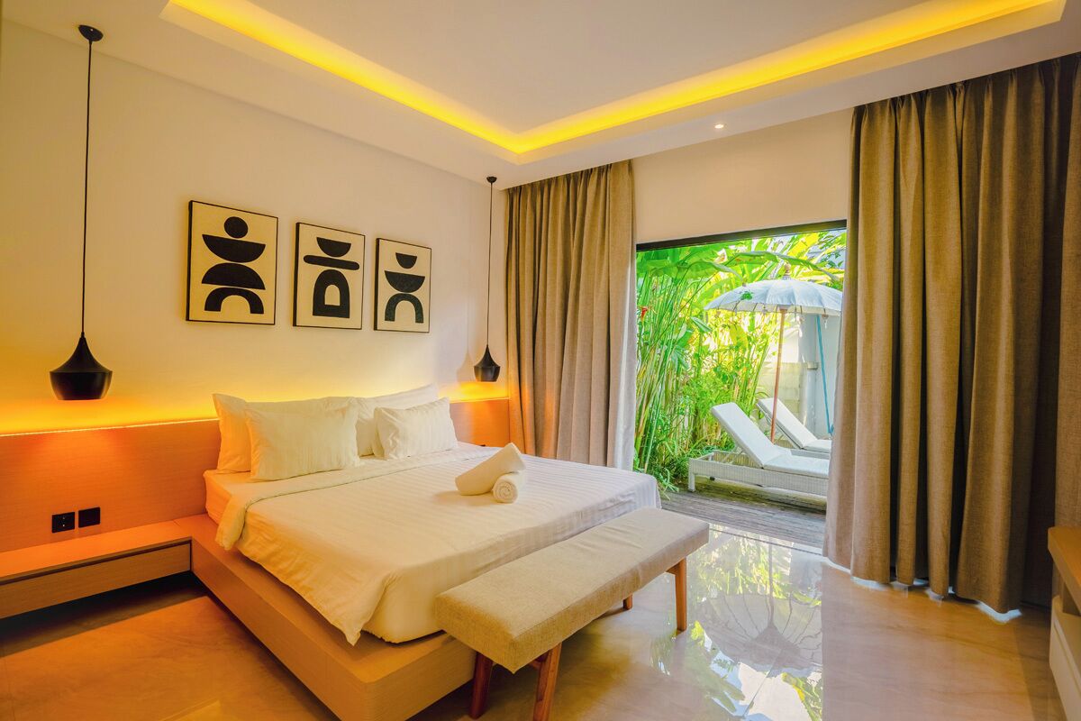 Quarto moderno com cama, abajures, obras de arte e vista para o verde lá fora.