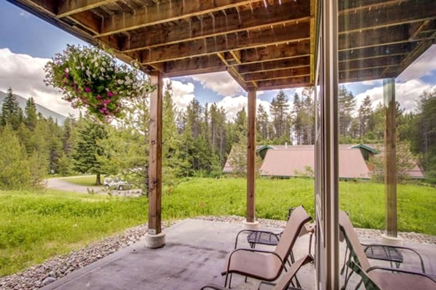 A covered outdoor area with chairs, a hanging flower arrangement, and a view of a forested landscape.