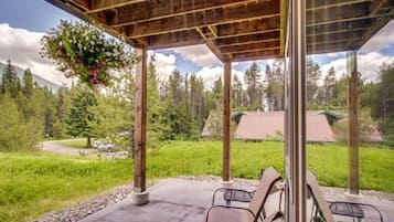 A covered outdoor area with chairs, a hanging flower arrangement, and a view of a forested landscape.