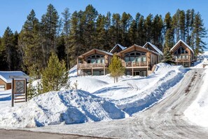 Ein Skigebiet mit mehreren Holzhütten, einer verschneiten Piste und einem klaren Himmel.