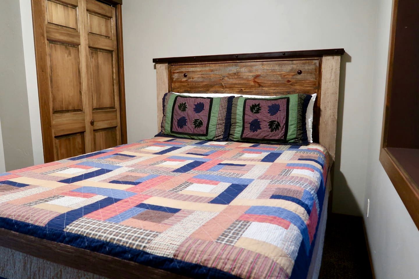 A bed with a wooden headboard and a colorful quilt.