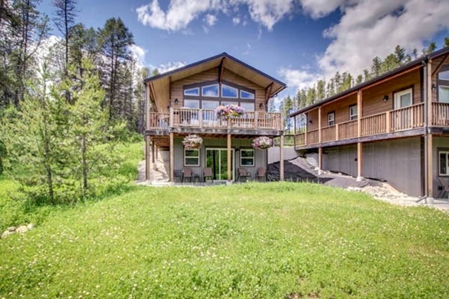 En toetagers hytte med balkon, overdækket terrasse og udsigt over den omkringliggende skov.