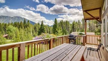 A wooden deck with a grill and a table, overlooking a forest and mountains.