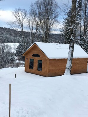 A wooden cabin with a snow-covered roof, surrounded by trees and a snowy landscape.