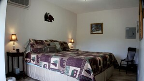 A bedroom with a large bed, two bedside lamps, a chair, a picture on the wall, and a heater on the wall.
