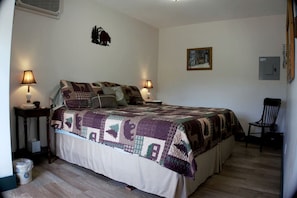 A bedroom with a large bed, two bedside lamps, a chair, a picture on the wall, and a heater on the wall.