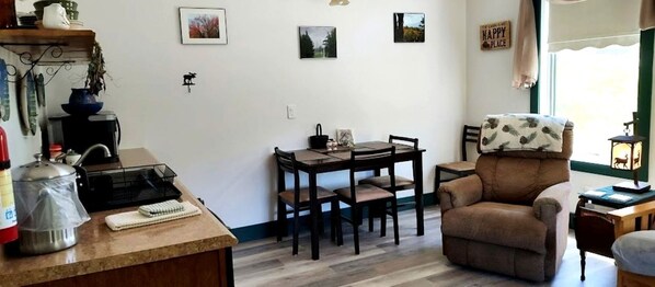 A cozy living room with a dining table, a comfortable armchair, and a bookshelf.