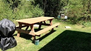 A picnic table with a grill and a covered item, surrounded by greenery.