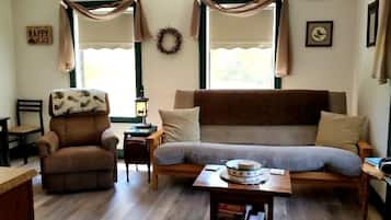 A cozy living room with a brown sofa, a brown armchair, a wooden coffee table, a small table with a bowl, and a wall clock.