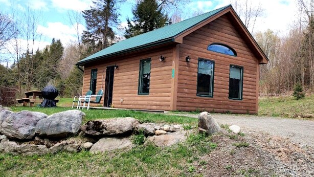 A log cabin with a green roof, a front porch, and a gravel driveway.