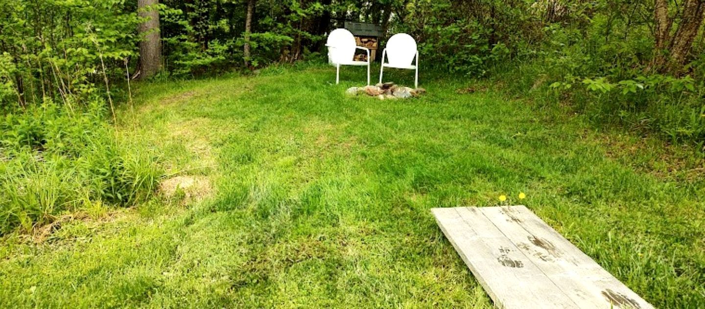 A grassy outdoor area with a wooden bench and two white chairs.