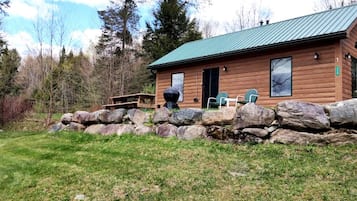 A wooden cabin with a stone wall, a picnic table, and two chairs.