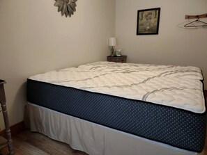 Un dormitorio con una cama, una mesita de noche, una lámpara de pared y un cuadro enmarcado.