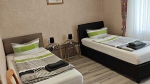 A hotel room with two beds, a chair, a small table, and a framed picture on the wall.