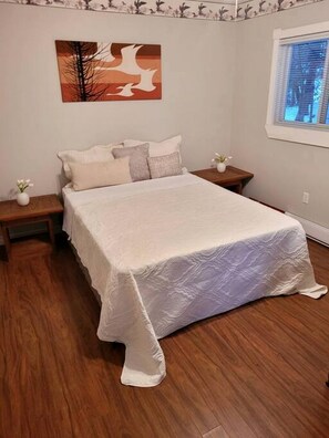 Ein Schlafzimmer mit einem großen Bett, zwei Nachttischen, einem Fenster mit Jalousien und einem an der Wand befestigten Kunstwerk.