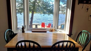 A dining area with a wooden table and chairs, large windows with a view of a lake and dock. - Spacious Family Cottage with Stunning Sunset Views on Sturgeon Lake, Near Bobcaygeon, Ontario (Kawartha Lakes)