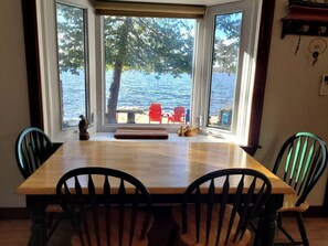 Ein Essbereich mit Holztisch und Stühlen, große Fenster mit Blick auf einen See und einen Steg.
