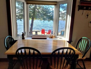 Un comedor con mesa y sillas de madera, ventanas amplias que dan a una vista de un lago y un embarcadero.