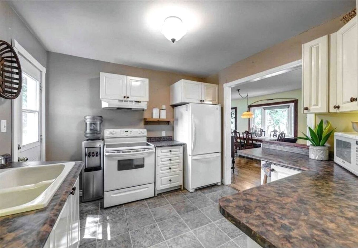 A kitchen with white appliances, a granite countertop, and a dining area with a view.