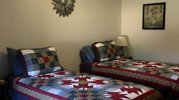A room with two beds, a wall clock, a decorative wall piece, and a framed picture.
