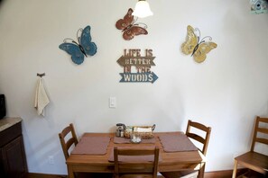 Un comedor con una mesa de madera, cuatro sillas, un letrero en la pared y mariposas decorativas.