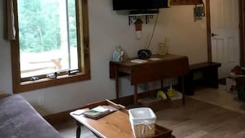 Uma sala de estar com sofá, uma mesa com cesta, TV na parede e janela com cortinas.