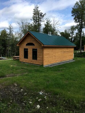 Una petita cabana de fusta amb teulada verda, una porta i una finestra petita.