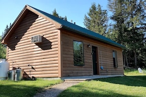Une cabane en rondins avec un toit à deux versants, une porte et une fenêtre.