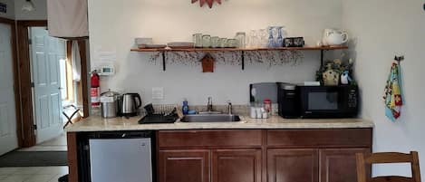 Una cocina equipada con lavavajillas, microondas y pileta. Hay una silla de madera y un tapete azul.